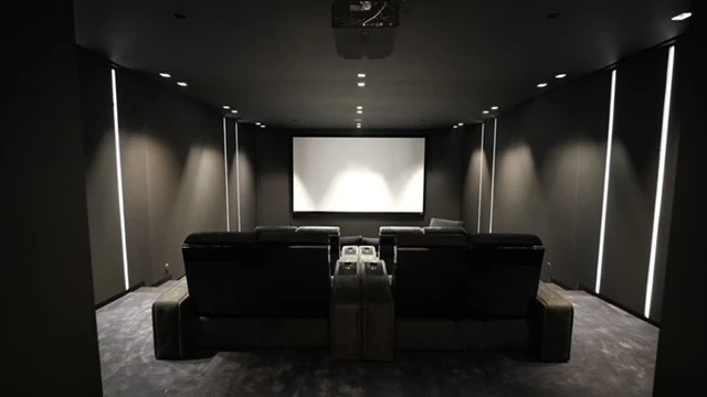 A dimly lit home theater featuring plush black seating and a large screen at the front, surrounded by sleek, dark walls.