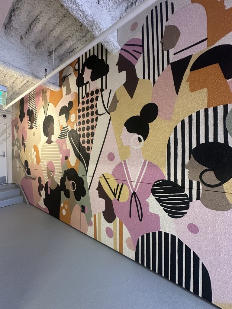 A vibrant mural depicting diverse women's silhouettes in various patterns and colors, enhancing a modern indoor space.