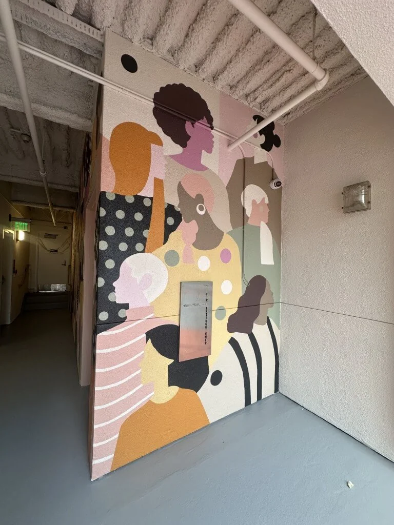 A vibrant mural depicting diverse silhouettes and faces in pastel colors, enhancing the hallway's artistic atmosphere.